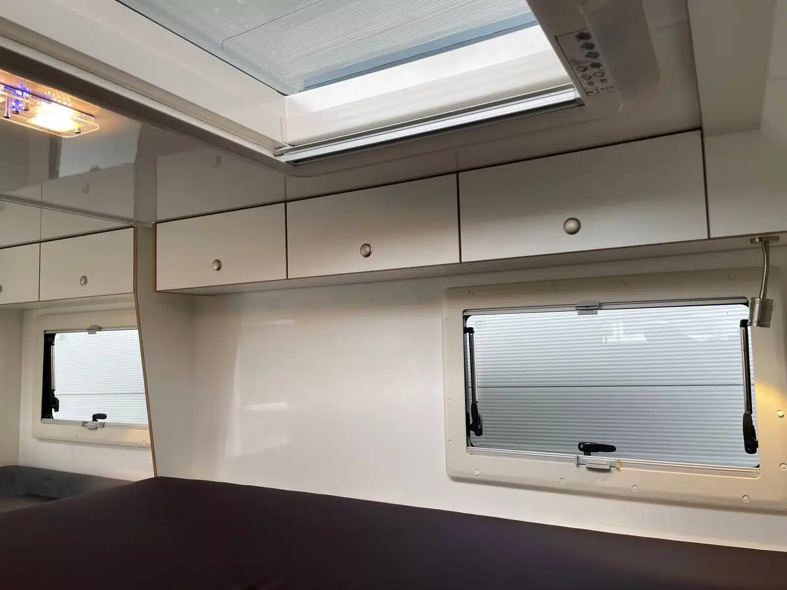 Schlafbereich im Wohnaufbau des Woelcke Autark Hilux mit Bett, Oberschränken und Fenstern