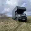 Das Allrad-Reisemobil Woelcke Autark Iveco XL 01 auf einer Wiese mit unebenem Untergrund unter wolkigem Himmel.