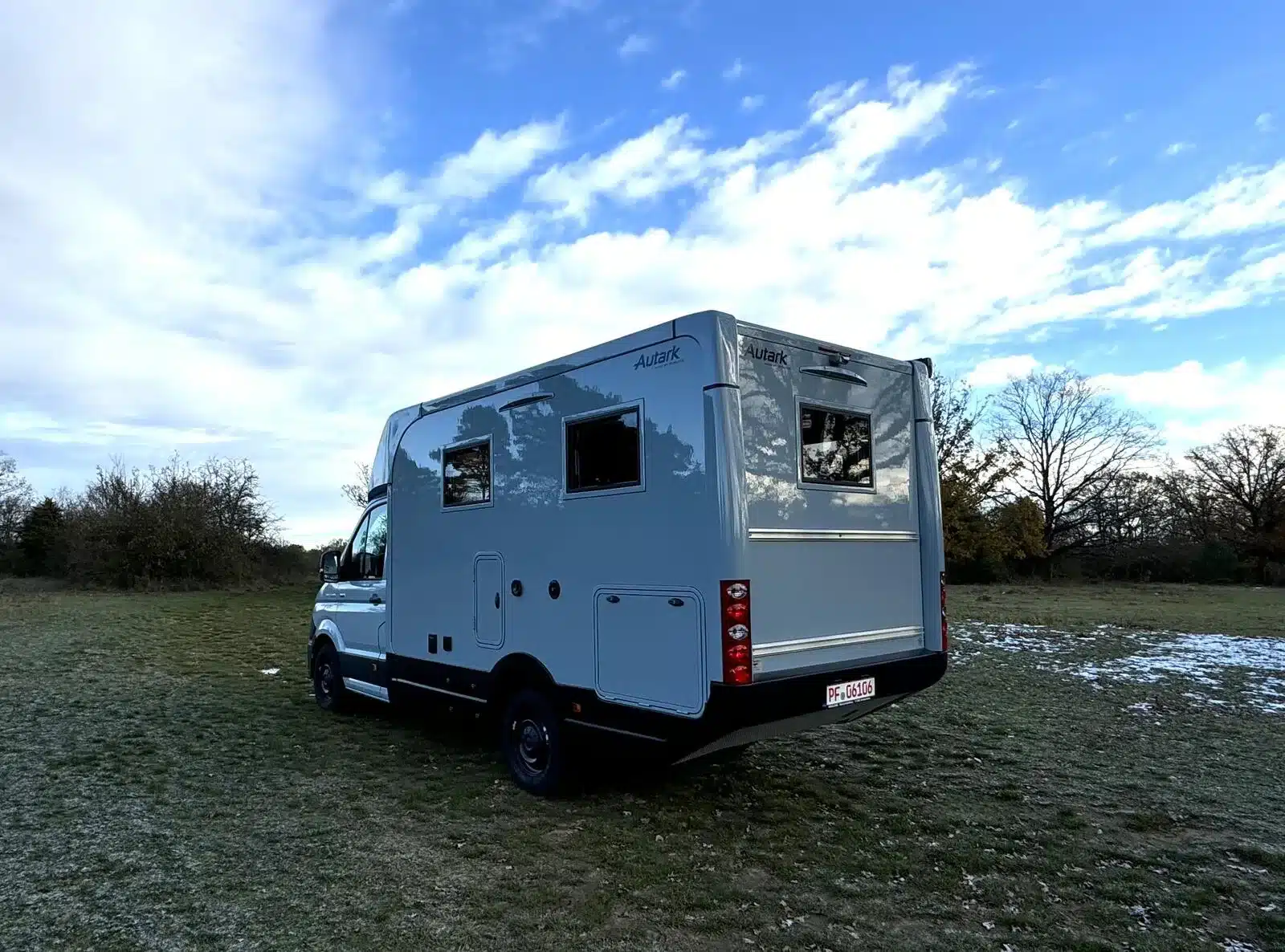 Das Woelcke Autark MAN TGE C9 Allradwohnmobil stehend auf einer Wiese, fotografiert von hinten seitlich bei blauem Himmel.