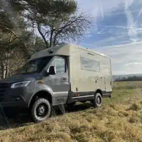 Woelcke Autark runner R10 Allrad-Wohnmobil, naturfarben, Mercedes Sprinter-Basis, auf einer Wiese vor Bäumen, Offroad-Reisemobil