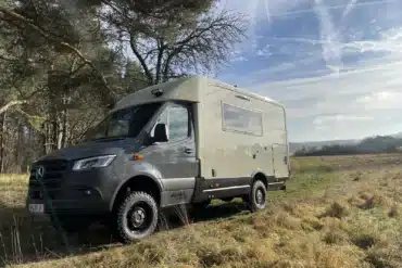 Woelcke Autark runner R10 Allrad-Wohnmobil, naturfarben, Mercedes Sprinter-Basis, auf einer Wiese vor Bäumen, Offroad-Reisemobil