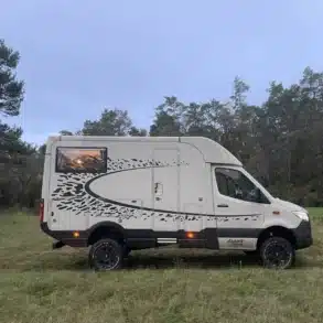 Seitenansicht des Woelcke Autark runner R4 Allrad-Campers auf einer Wiese mit Wald im Hintergrund.