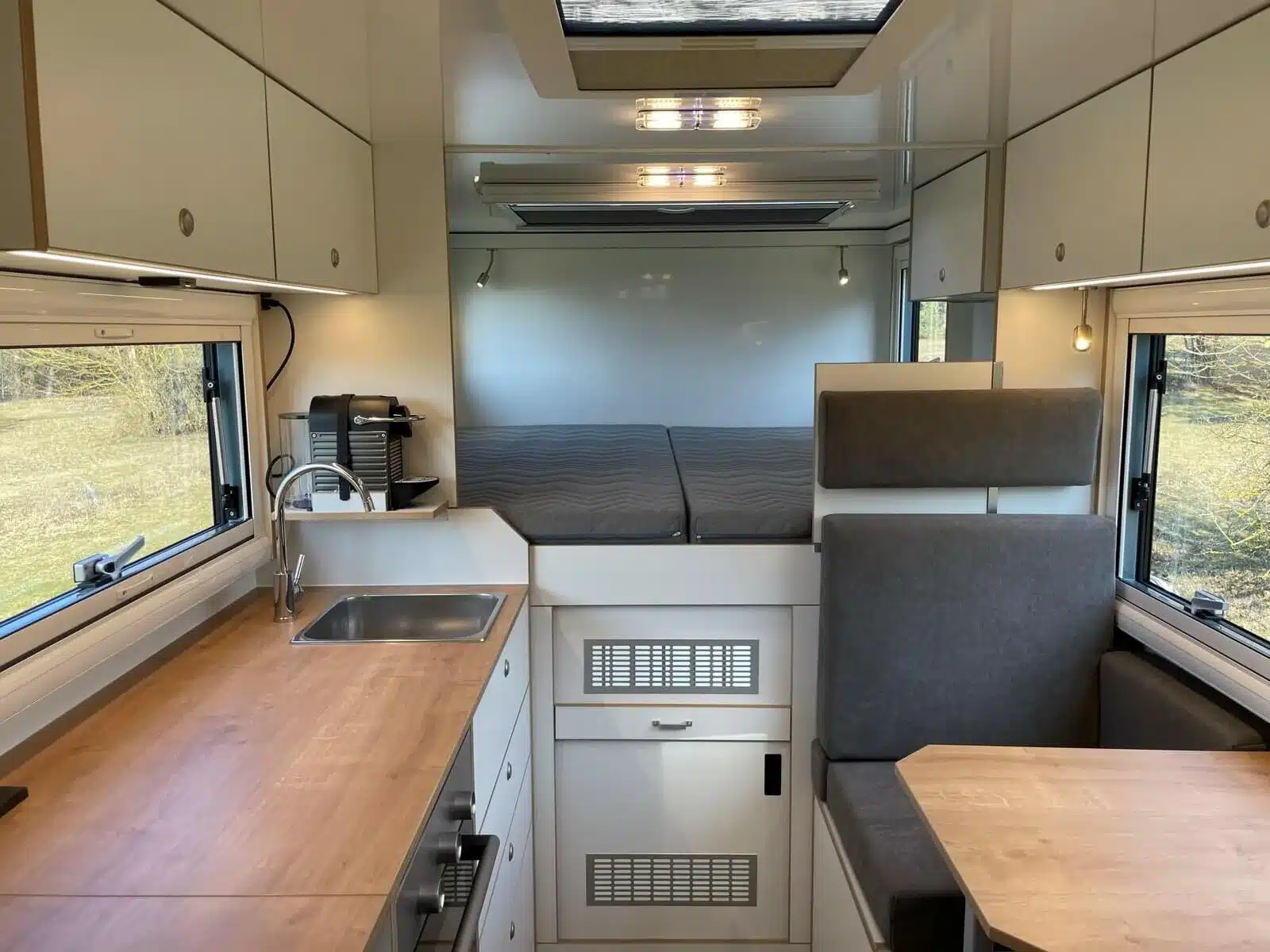 Wohnbereich des Woelcke Autark runner R6-lang 2023 mit Küchenzeile, Sitzgruppe und großzügigem Bett im Hintergrund.
