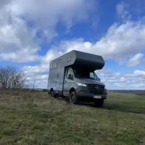 Wohnmobil Woelcke Autark runner XL 01 2024, Mercedes-Benz Sprinter 519CDI 4x4, parkt auf einer Wiese bei bewölktem Himmel.