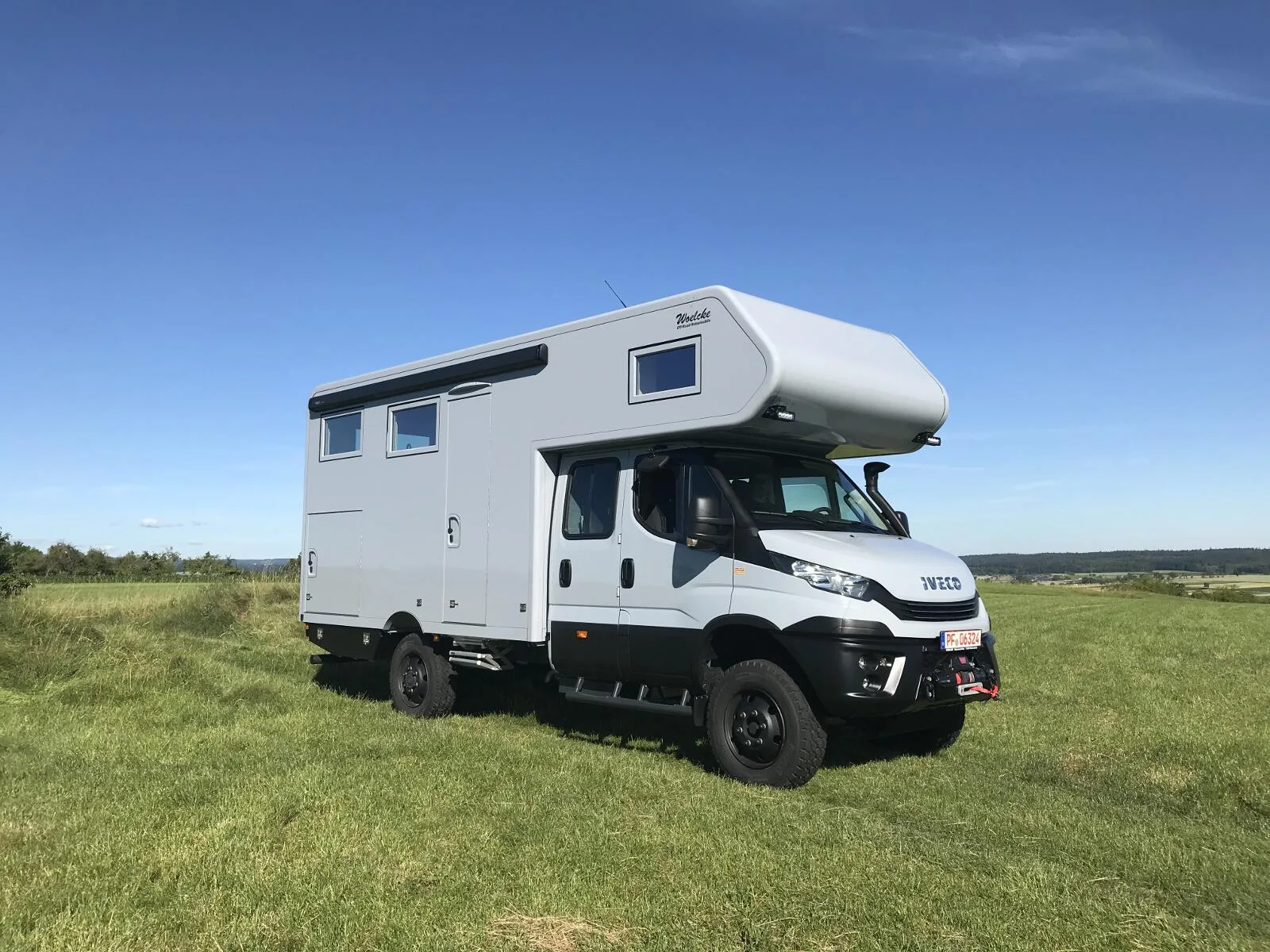Weißer Iveco Daily 4x4 Doka mit Woelcke GFK-Wohnaufbau auf einer grünen Wiese