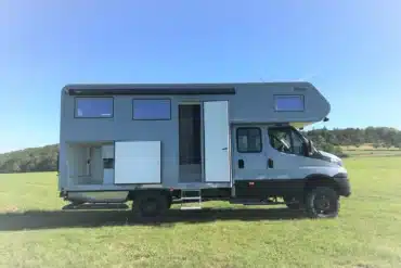 Iveco Daily 4x4 Doka mit grauem Woelcke GFK-Wohnaufbau auf einer Wiese