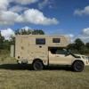 Seitenansicht des Woelcke Toyota Hilux Extra Cap 4x4 Camper auf einer Wiese unter bewölktem Himmel.