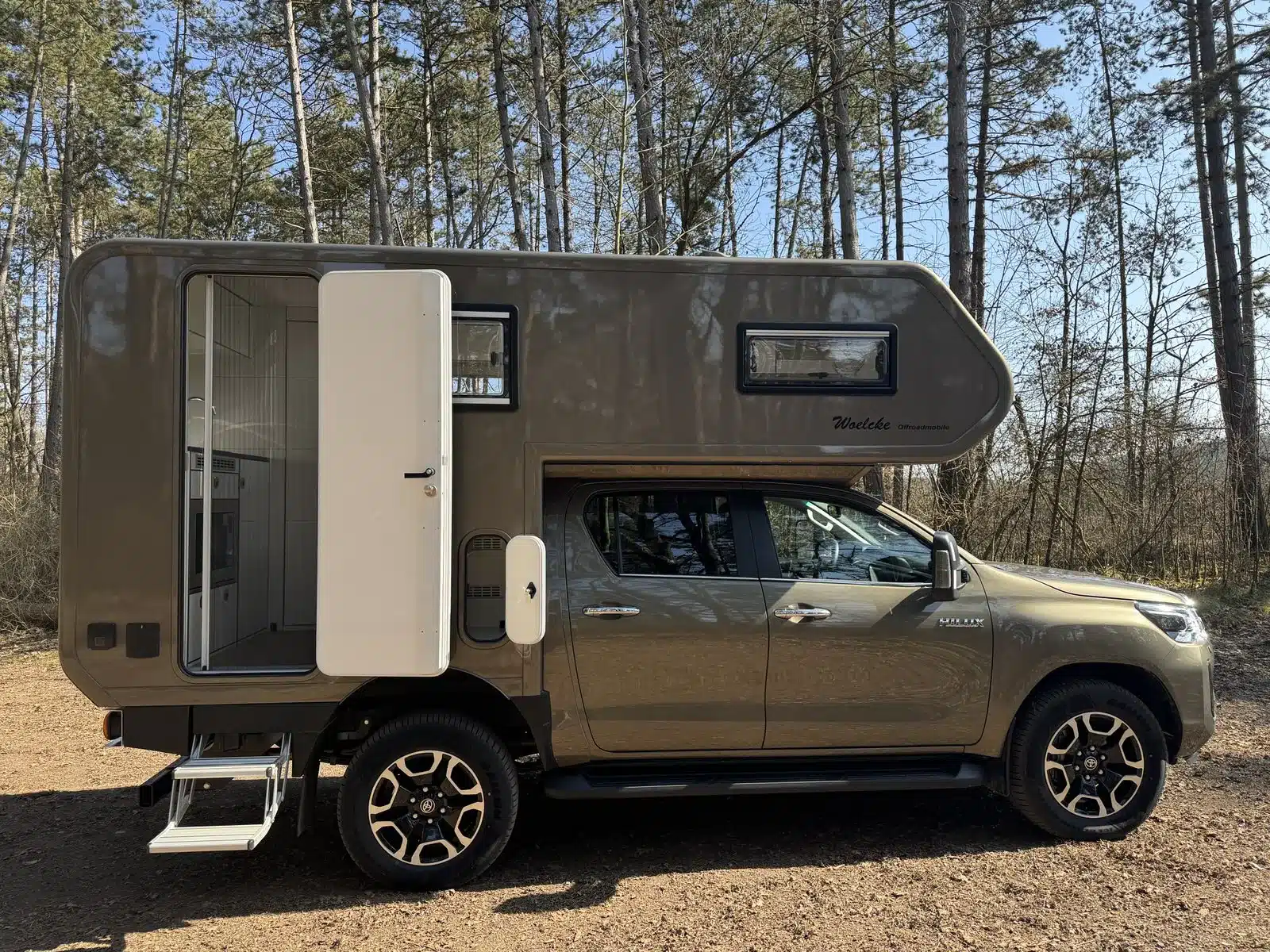 Seitlich aufgenommenes Woelcke Offroadmobil auf Basis eines Toyota Hilux mit GFK-Wohnaufbau im Wald