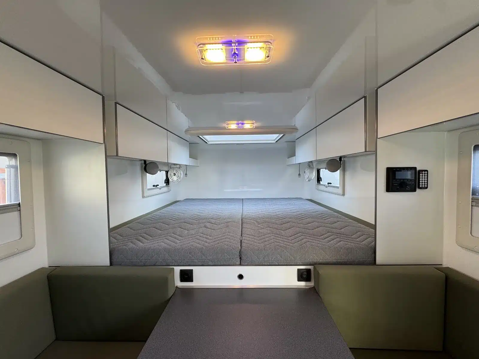 Innenraum des Woelcke Toyota Hilux 4x4 mit breitem Doppelbett, Oberschränken, Fenstern und Innenbeleuchtung