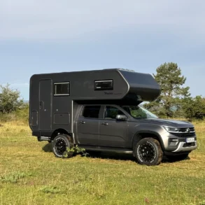 Woelcke VW Amarok 2024 Offroad-Camper in dunkler Ausführung mit Alkoven im Grünen
