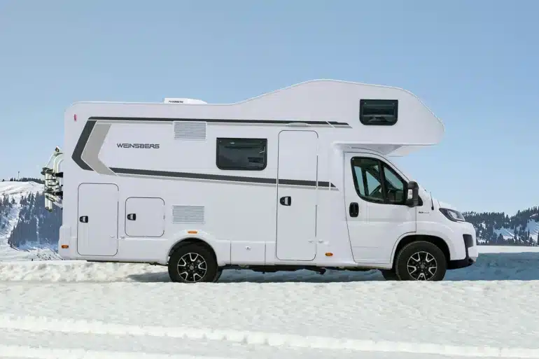 Seitenansicht des WEINSBERG CaraHome Alkovens auf schneebedecktem Untergrund vor winterlicher Kulisse