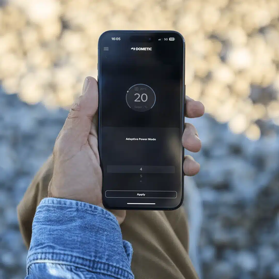 Hand hält Smartphone mit geöffneter Dometic-App zur Steuerung der FreshJet FJZ7 2600 Dachklimaanlage