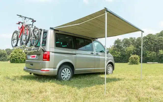 VW T5 mit geöffneter Fiamma F40 Van Dachmarkise auf einer Wiese, Fahrräder am Heckträger.