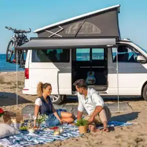 Campingbus mit ausgefahrener Fiamma F45s Wandmarkise, darunter ein Picknick am Strand