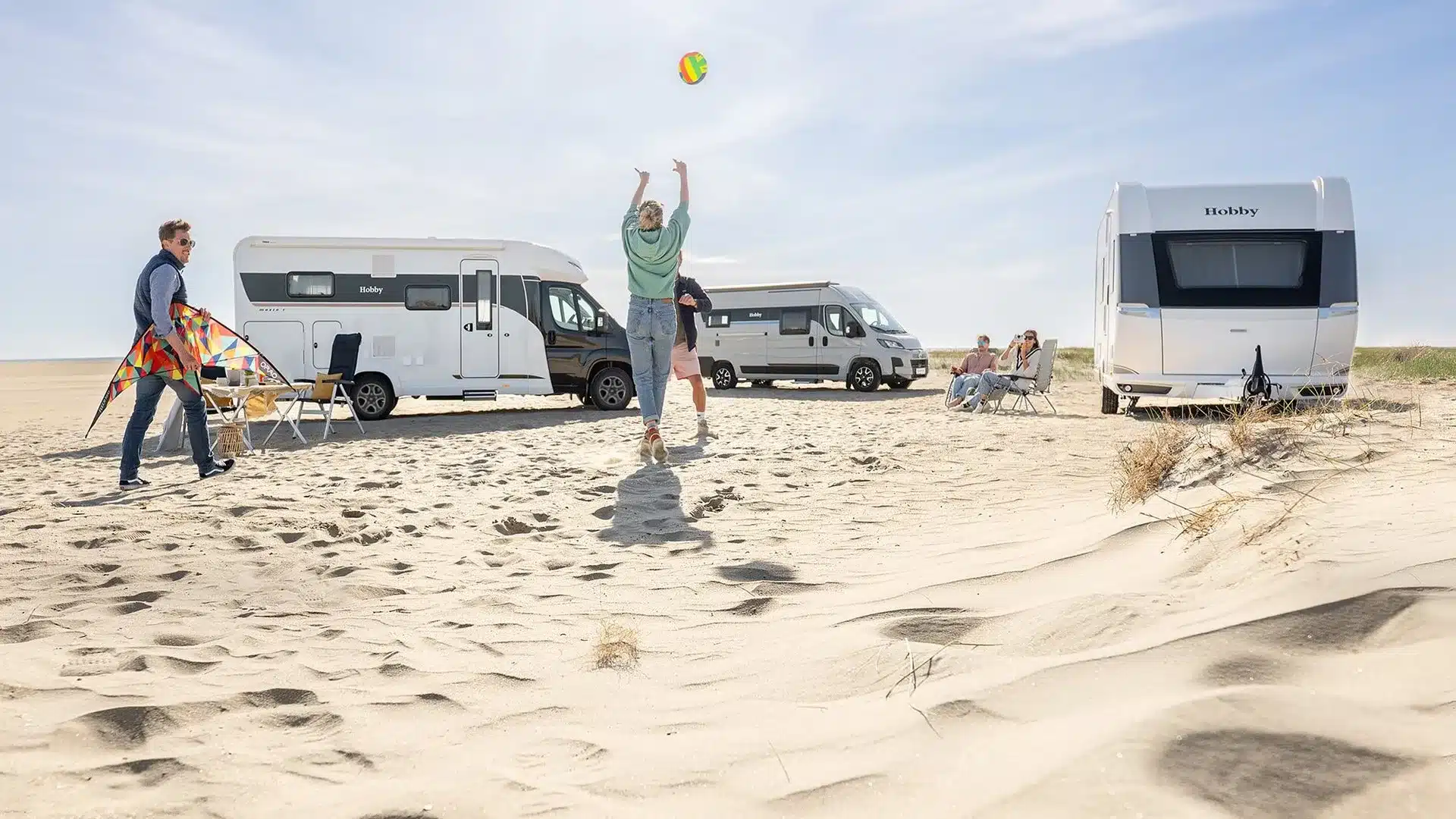 Hobby PRESTIGE VAN zusammen mit weiteren Freizeitfahrzeugen am Sandstrand, Personen genießen die Zeit draußen