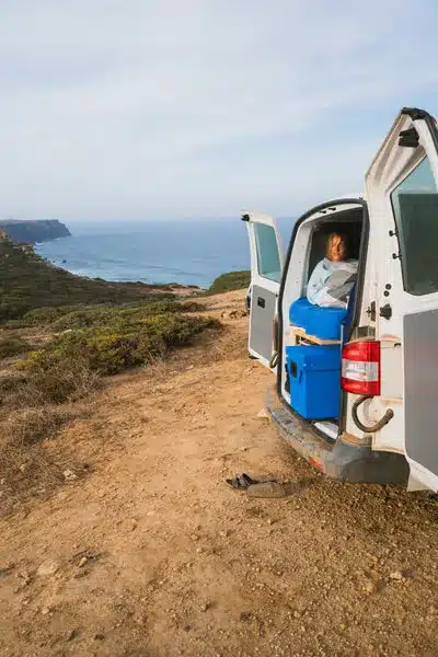 Blau-silberne QOOL Box Original im offenen Campingvan am Meer, Person sitzt entspannt dahinter