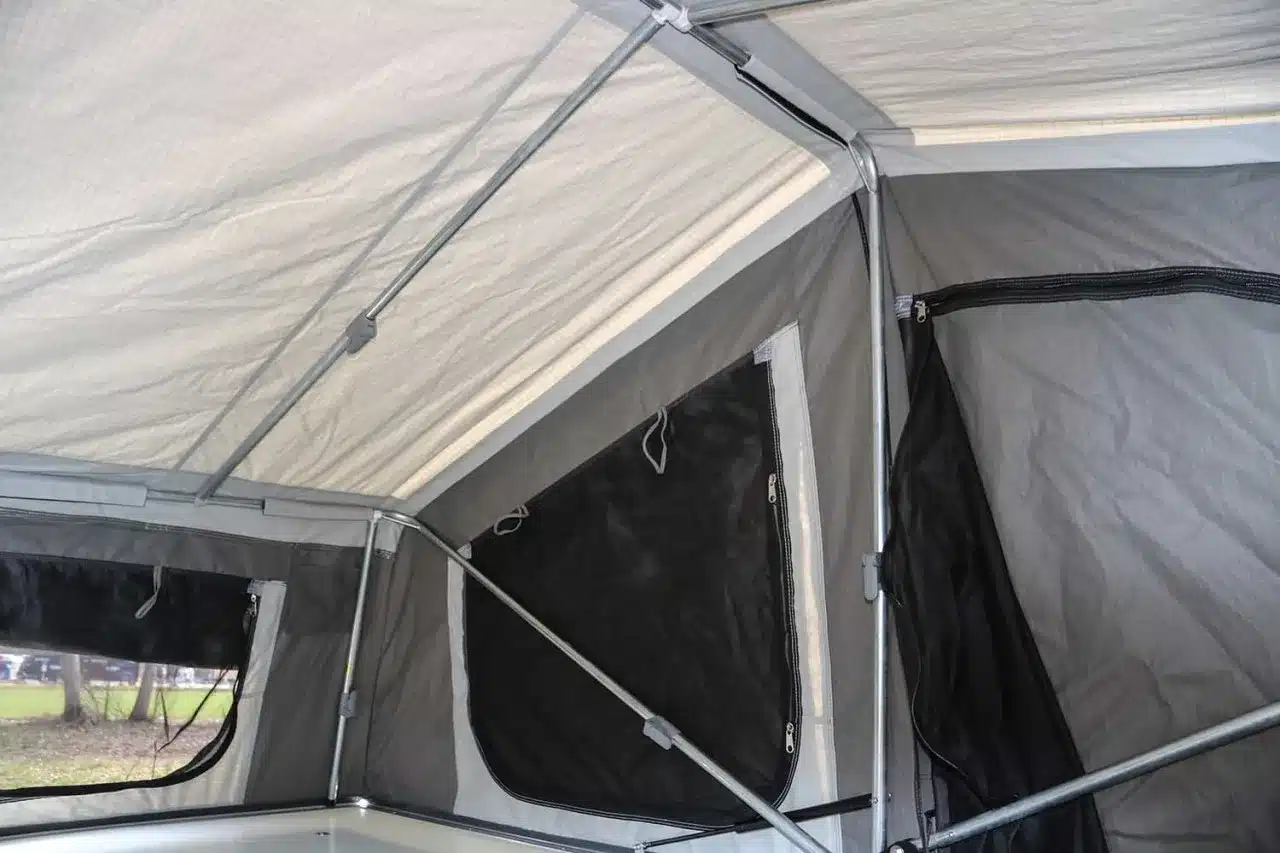 Innenraum eines aufgebauten Anhängerzelts mit Stahlgestänge und seitlichen Fenstern.