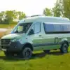 Grüner Westfalia James Cook 600 D Kastenwagen auf Mercedes Sprinter Basis steht auf einer Wiese vor Bäumen und einem See.