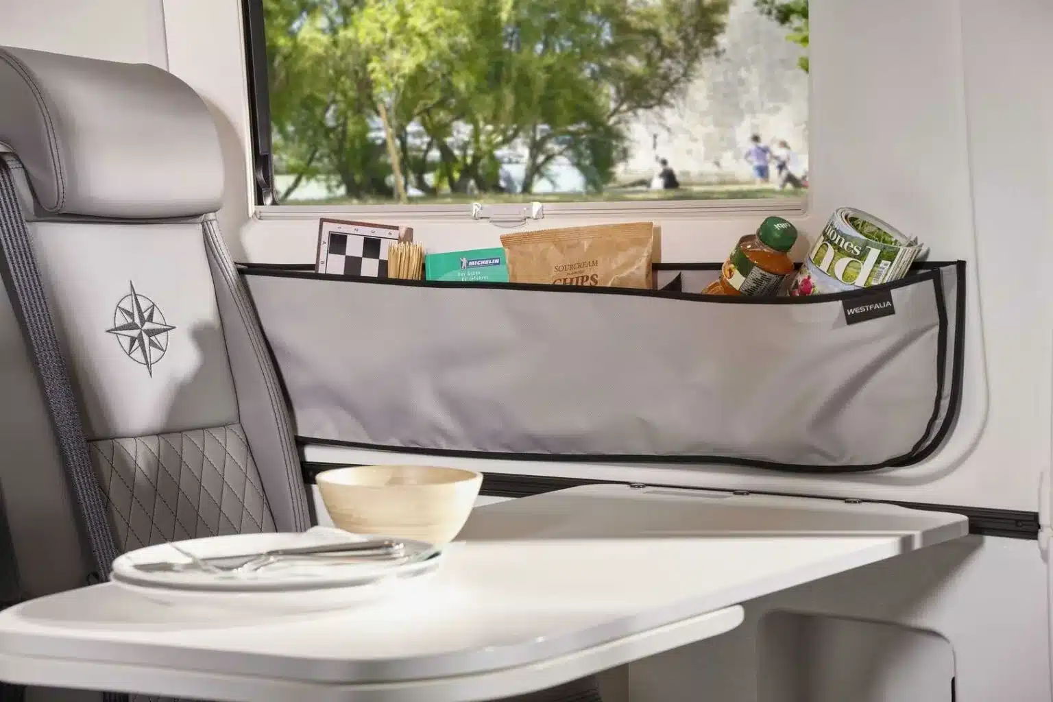Innenraum des Westfalia Meridian mit Sitzbank, Esstisch und seitlicher Stauraumtasche mit Reiseutensilien.