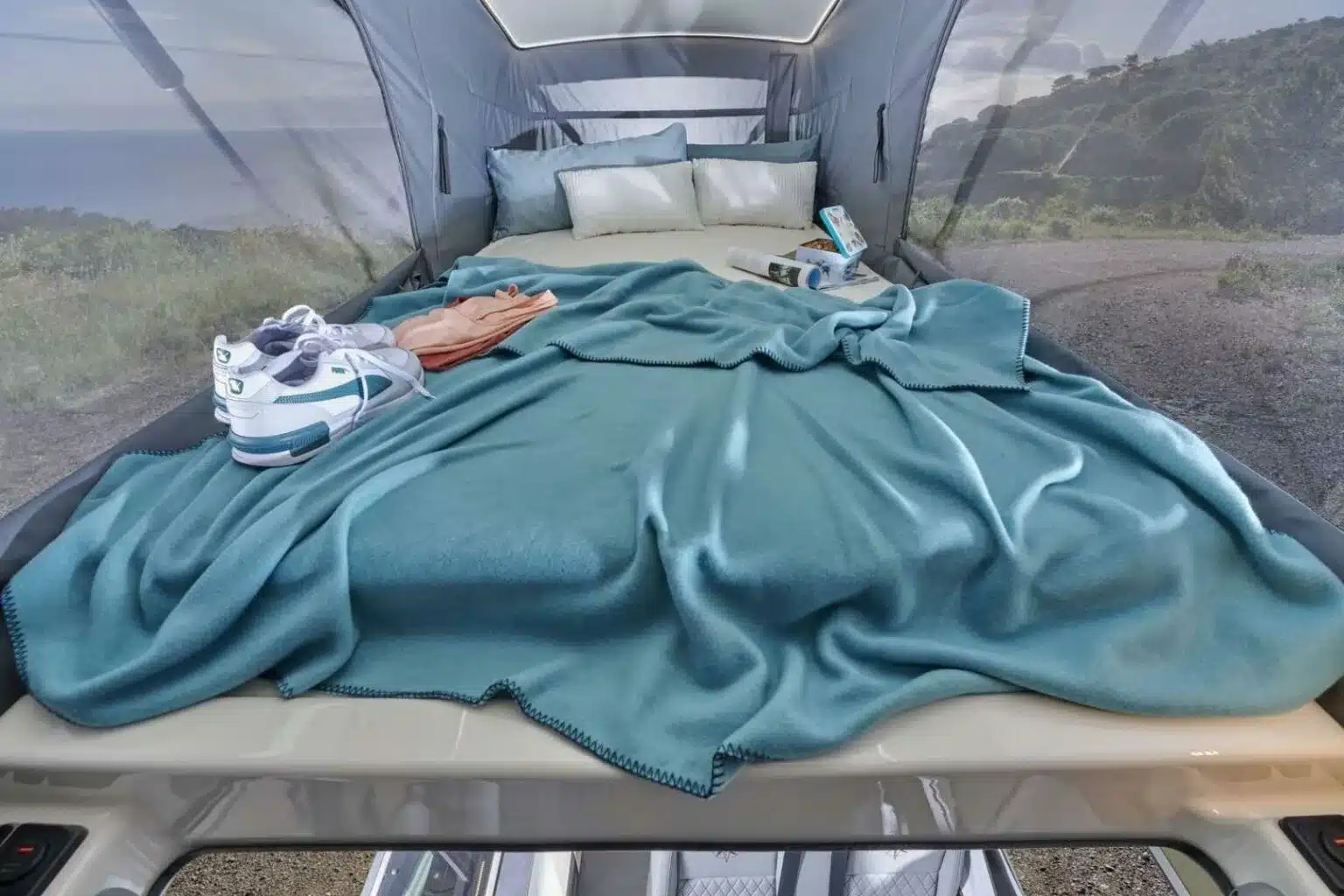 Das große Bett im optionalen Aufstelldach des Westfalia Meridian, ausgestattet mit blauer Decke und bequemen Kissen.