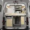 Heckansicht des Ahorn Camp Van 560 mit aufgeklapptem Doppelbett und Stauraumbereich darunter.