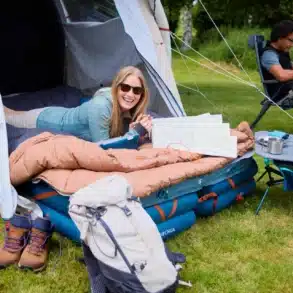 QUECHUA Campingbett Bed Air 70x200 cm im Zelt, darauf eine Person mit Karte, Campingausrüstung außen