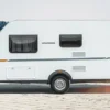 WEINSBERG CaraCito Caravan steht auf einem gepflasterten Platz mit Blick auf einen See und Waldlandschaft