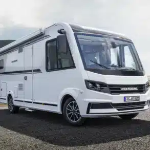 Außenansicht des WEINSBERG CaraCore Wohnmobils mit großer Panorama-Frontscheibe auf einer Straße vor Bergkulisse.