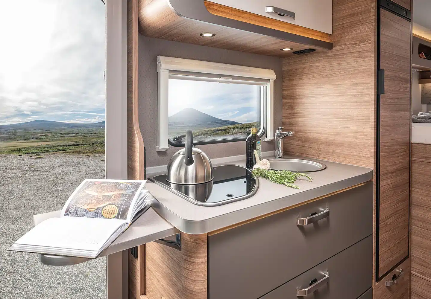 Küchenzeile mit Kochfeld, Spüle, Kräutern und Blick durch das Fenster im WEINSBERG CaraCore Wohnmobil