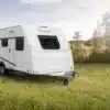 WEINSBERG CaraLife Caravan steht auf einer grünen Wiese bei Sonnenschein.