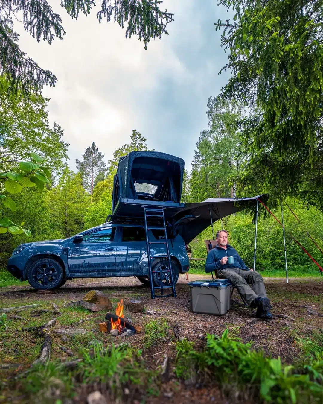 Dacia Duster mit aufgestelltem Dachzelt und Markise auf einem Waldcampingplatz