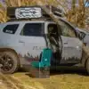 Portable Verschweißtoilette vor einem mit Dachgepäck und Dachzelt ausgestatteten Dacia Duster