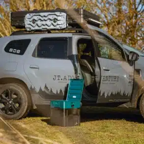 Portable Verschweißtoilette vor einem mit Dachgepäck und Dachzelt ausgestatteten Dacia Duster