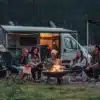 CROSSCAMP EXPLR Campervan mit geöffnetem Aufstelldach und Menschen beim Camping am Lagerfeuer