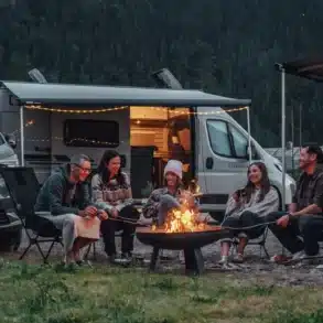 CROSSCAMP EXPLR Campervan mit geöffnetem Aufstelldach und Menschen beim Camping am Lagerfeuer