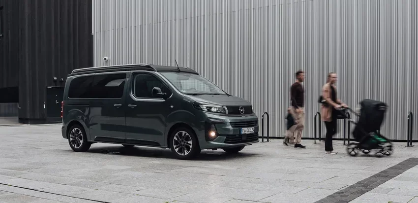 CROSSCAMP EXPLR 5.0 F Opel Camper-Van vor moderner Gebäudefassade in der Stadt, Seitenansicht.