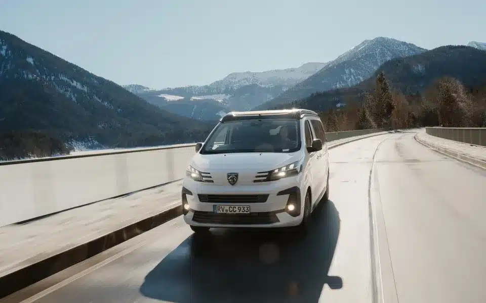 Weißer CROSSCAMP EXPLR Campervan auf winterlicher Straße mit Bergen im Hintergrund.