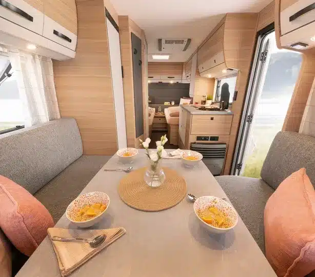 Modern eingerichteter Innenraum des Dethleffs Summer Edition 460 EL mit Sitzgruppe, Tisch, Küche und Einzelbetten im Hintergrund