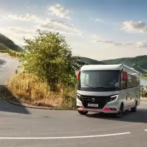Niesmann+Bischoff iSmove 2027 Reisemobil fährt auf einer Straße durch hügelige Landschaft.