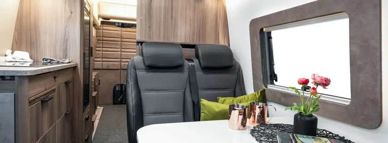 Modern eingerichteter Wohn- und Essbereich im KABE Abisko Van 690 LB mit Tisch, Sitzbänken, Fenster und Blick auf die Küche.
