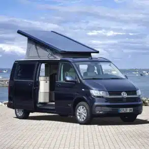 Westfalia Kepler One Campervan mit Aufstelldach und geöffneter Schiebetür vor einer Küstenkulisse.