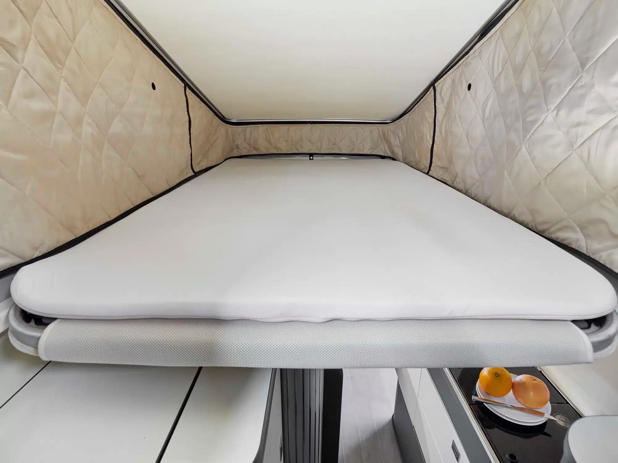 Innenansicht des Dachbetts im Aufstelldach des Westfalia Kepler One Campervans mit weißer Matratze und hellen, gesteppten Seitenwänden.