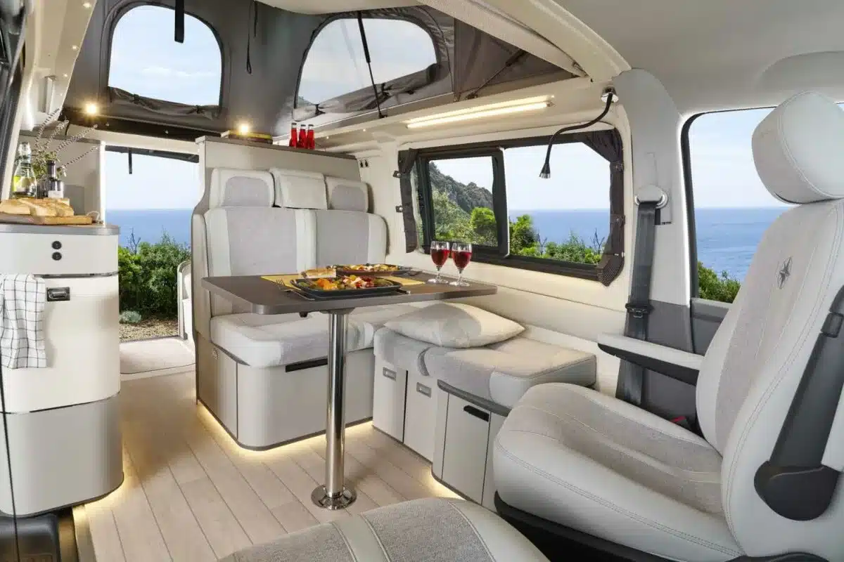 Innenraum des Westfalia Kepler One Campervans mit Sitzlandschaft, Esstisch, geöffneter Seitentür und Blick auf das Meer