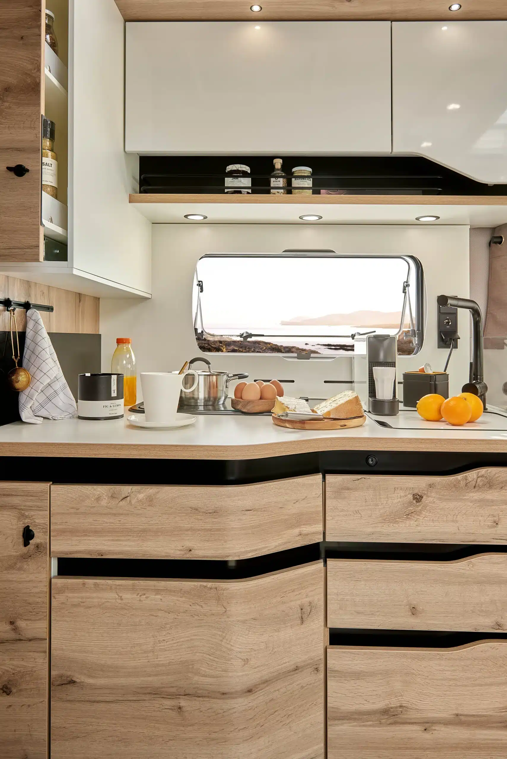Moderne Küchenzeile mit Holzfronten und weißem Oberschrank im LE VOYAGEUR LV8.5CF Wohnmobil, Frühstückszubereitung mit frischen Zutaten