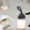 LUVO LED Campingleuchte leuchtet auf einem Campingtisch neben Weingläsern und Tellern.