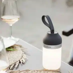LUVO LED Campingleuchte leuchtet auf einem Campingtisch neben Weingläsern und Tellern.