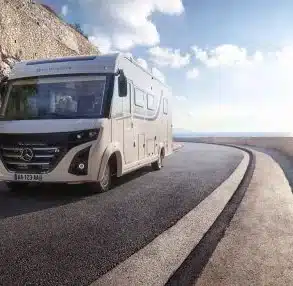 Le Voyageur LVXH7.6 GJF fährt auf einer kurvigen Küstenstraße unter blauem Himmel.