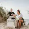 Der MAVERIQ® Z Kartuschen-Gaskocher im Einsatz beim Kochen am Strand, zwei Personen sitzen in den Dünen, kochen und genießen die Natur