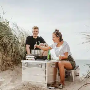 Der MAVERIQ® Z Kartuschen-Gaskocher im Einsatz beim Kochen am Strand, zwei Personen sitzen in den Dünen, kochen und genießen die Natur