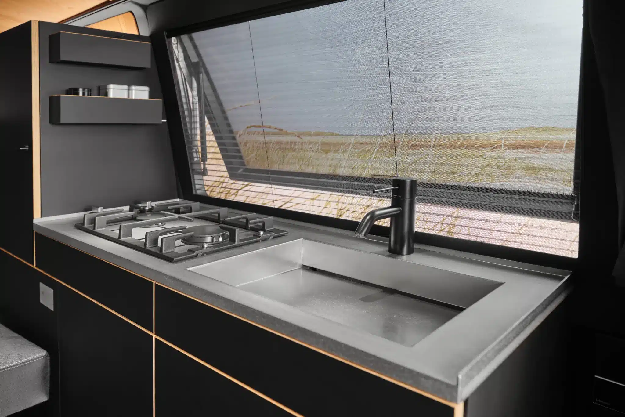 Minimalistische Küchenzeile aus Edelstahl mit Spüle, Gaskochfeld und mattschwarzer Armatur im Campervan Moormanns Holzklasse 2.0.